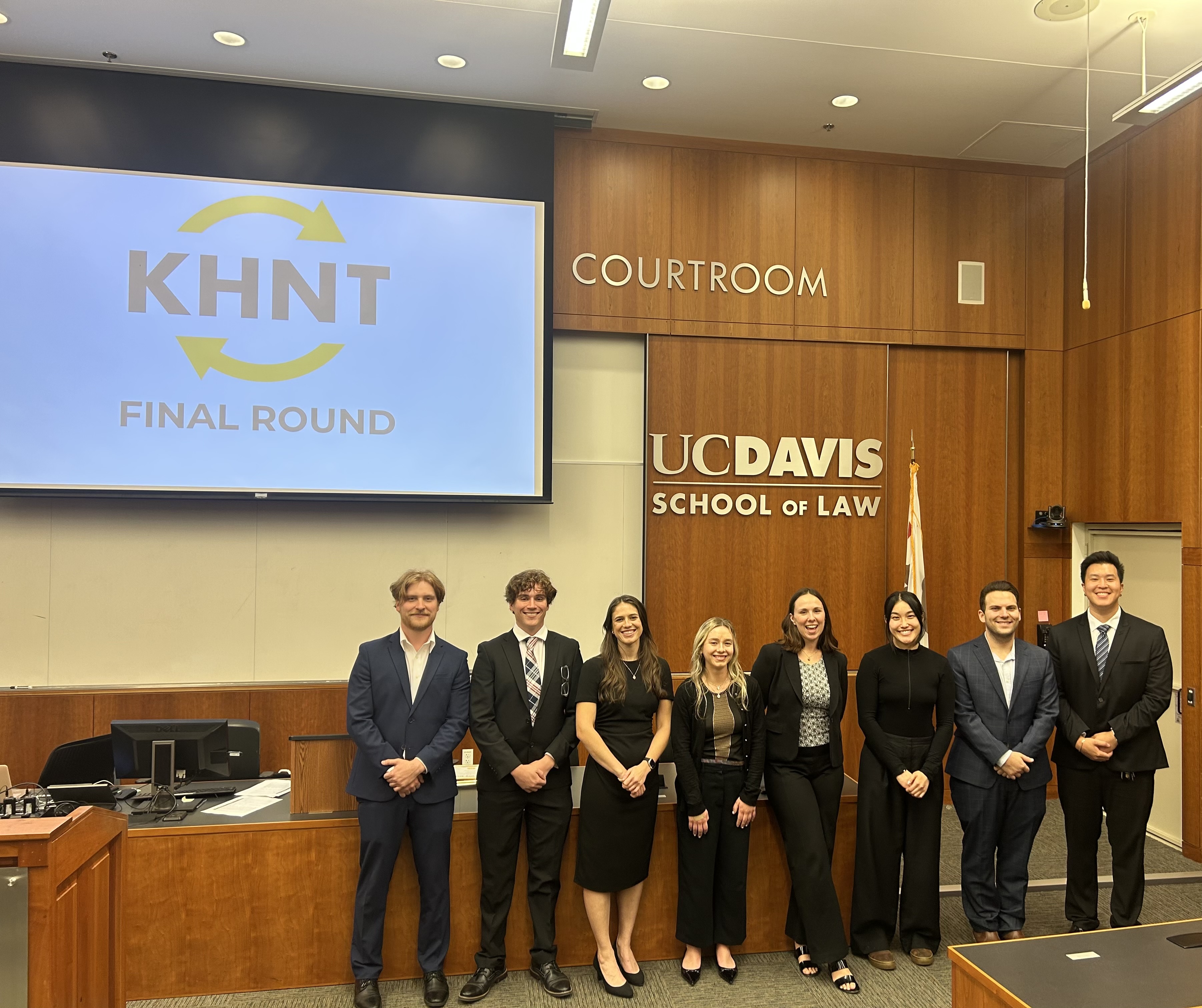 From left to right, Class of 2028 students Evan Gaudreau, Carter Dalke, Rory Yoakum, Lauren Tepper, Anna Bullock, Emily Ma, Nathan Nemeth, and Garrett Chao. The students are wearing professional clothing and are standing in a line in the front of the King Hall courtroom. 