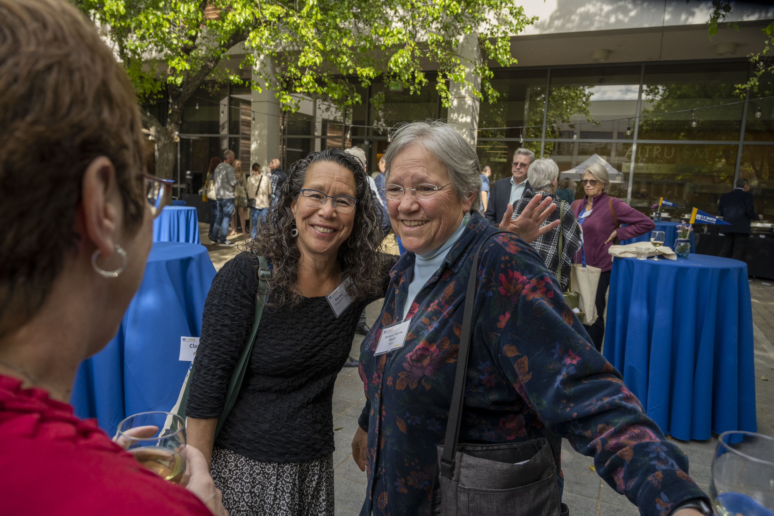 Two women smiling and posing at outdoor reception with blue cocktail tables