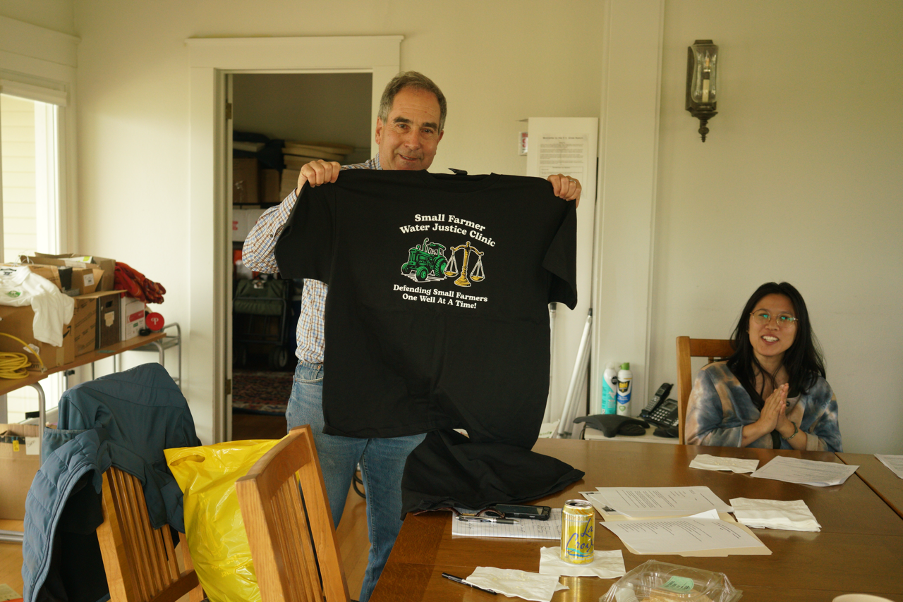 Professor David Sandino holding a Small Farmer Water Justice Clinic t-shirt.