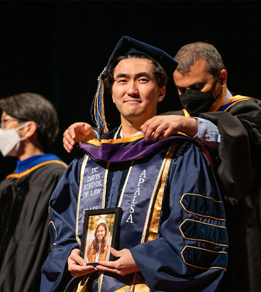 A UC Davis Law student from the Class of 2022 gets hooded by a faculty member on Commencement Day.