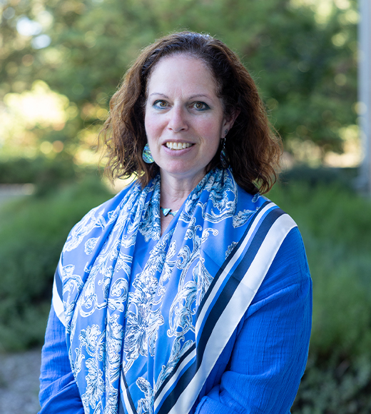 Darcie Houck wearing a blue blouse and scarf. She is smiling at the camera.