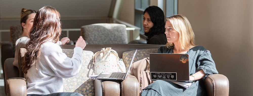 Three women chatting in a sunlit lounge.