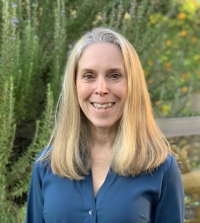 CELPC co-director Tracy Winsor wearing a blue blouse. She is smiling at the camera and there are green trees behind her.